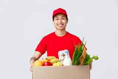 在线购物食物交付互联网商店概念快乐的微笑亚洲的家伙红色的帽t恤持有盒子新鲜的食品杂货站客户通过员工交付产品