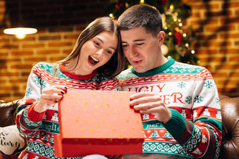 肖像浪漫的夫妇开放现在礼物盒子晚上装饰圣诞节树快乐男人。使圣诞节礼物亲爱的女人概念假期浪漫惊喜