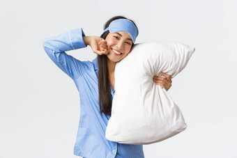 很高兴美丽的亚洲女孩蓝色的睡衣睡觉面具说谎床上拥抱枕头微笑满意度伸展运动感觉好晚上睡眠白色背景