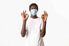 肖像满意非裔美国人英俊的的家伙医疗面具无檐小便帽住受保护的科维德流感大流行显示手势站白色背景