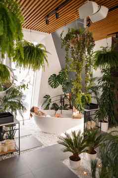 放松年轻的女人采取泡沫浴现代浴室装饰热带植物奢侈品水疗中心度假胜地