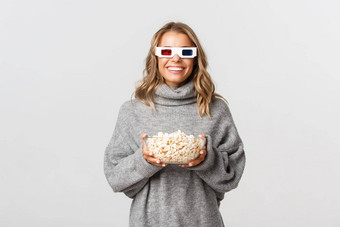 图像美丽的年轻的女人灰色毛衣看电影眼镜吃爆米花微笑快乐相机站白色背景