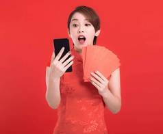 快乐中国人一年惊讶年轻的女人持有红色的信封幸运的看移动电话