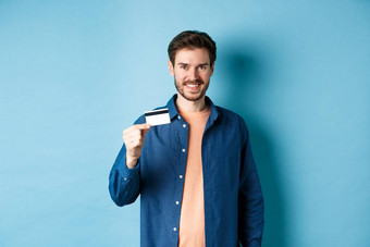 英俊的微笑的家伙显示塑料信贷卡满意站蓝色的背景