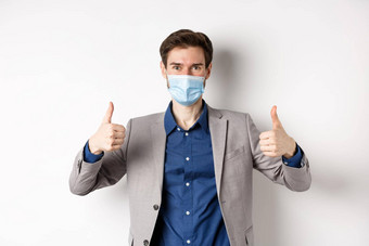 科维德流感大流行业务概念快乐的男人。西装医疗面具预防措施办公室显示拇指白色背景