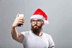 圣诞节假期技术人概念英俊的有胡子的男人。圣诞老人他采取自拍图片智能手机灰色背景