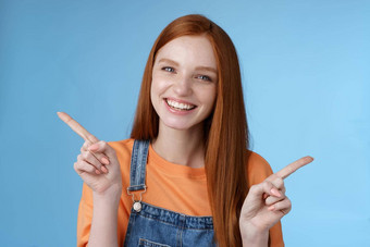 友好的快乐笑漂亮的红色头发的人女孩女学生显示很多机会建议使选择指出横盘整理左介绍产品咧着嘴笑很高兴蓝色的背景