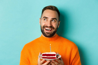 特写镜头快乐成人男人。庆祝生日持有bday蛋糕蜡烛使站绿松石背景