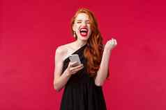 肖像成功的很高兴幸运的红色头发的人女孩赢得收到伟大的新闻消息礼物泵冠军尖叫并黑色的优雅的衣服红色的背景