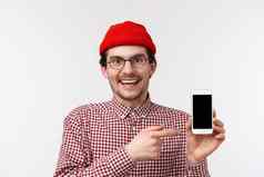 技术人概念特写镜头肖像快乐微笑年轻的有胡子的赶时髦的人的家伙持有移动电话指出智能手机显示推荐下载应用程序吹牛太棒了匹配