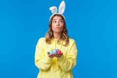 深思熟虑的可爱的高加索人女孩兔子耳朵思考思考梦幻持有复活节鸡蛋决定隐藏传统的假期游戏蓝色的背景