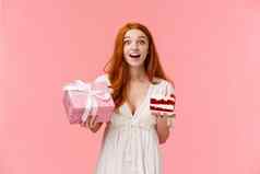 梦幻着迷一厢情愿的可爱的生日女孩红色的卷曲的头发白色衣服庆祝生日持有包装礼物和平生日蛋糕基斯蜡烛微笑惊讶