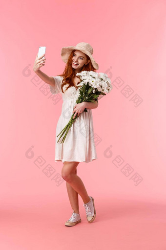 全身的垂直拍摄可爱的浪漫的愚蠢的红色头发的人女人享受美丽的春天一天持有花束花采取自拍智能手机微笑很高兴