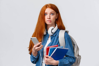 优柔寡断紧张可爱的红色头发的人大一新生女孩开始一年大学担心相机咬唇紧张地持有背包笔记本电脑智能手机阅读消息