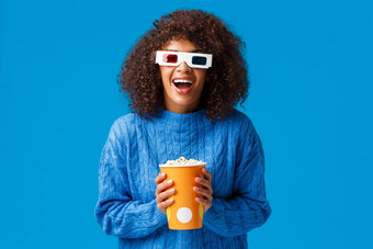 快乐的华丽的非裔美国人女人享受看电影电影笑微笑兴奋影响穿眼镜持有爆米花站蓝色的背景