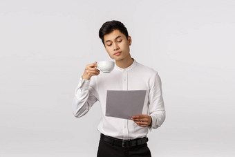 业务企业概念英俊的亚洲商人喝咖啡杯文档阅读报告研究图表工作办公室站白色背景专横的
