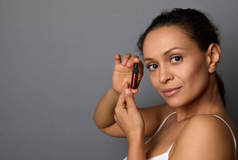 有吸引力的非洲美国女人完美的新鲜的清洁皮肤提出了灰色的背景持有玻璃Jar美产品水疗中心美容美治疗概念复制空间