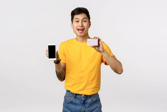 快乐微笑快乐的亚洲的家伙黄色的t恤纹身持有智能手机信贷卡推荐在线超市夜未眠<strong>金融</strong>系统订单产品<strong>互联网</strong>白色背景