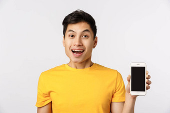 电话快乐的兴奋年轻的亚洲男人。黄色的t恤显示智能手机微笑喜欢过滤器应用程序推荐加入公司在线功能白色背景