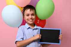 可爱的微笑小学生空空白黑板手站五彩缤纷的气球粉红色的背景复制空间