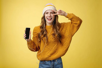 积极的无忧无虑的迷人的年轻的女孩显示和平手势穿《<strong>连线</strong>》杂志耳机显示智能手机屏幕促进应用程序很酷的品牌移动电话笑无忧无虑的黄色的背景