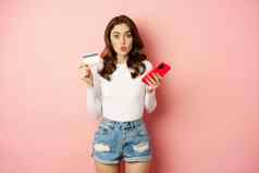 热情的女孩购物者持有信贷卡智能手机逗乐在线购物促销提供特殊的交易站粉红色的背景