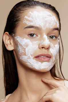 年轻的女人脸面具奶油清洁皮肤面部擦洗米色背景