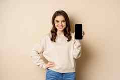 时尚的微笑女人显示智能手机屏幕移动应用程序接口站米色背景