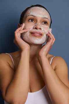 迷人的女人应用泡沫清洗化妆品产品脸按摩运动删除化妆让人耳目一新皮肤剥离素美产品孤立的灰色的背景