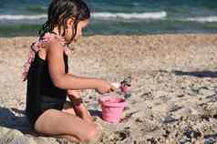 一边肖像学龄前儿童女孩持有耙填充粉红色的玩具桶沙子建筑桑迪形状城堡享受日光浴夏天假期