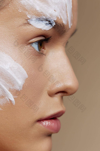 浅黑肤色的女人应用舒缓的脸面具化妆品米色背景一边视图