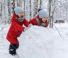 双胞胎女孩红色的夹克滚动巨大的雪球使雪人