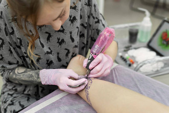 主纹身纹身工作室专业文身的人作品工作室女人粉红色的手套使纹身腿年轻的女孩