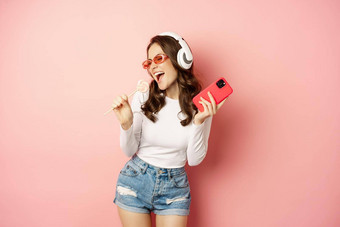 夏天女孩笑容易的萝莉波普听音乐耳机跳舞智能手机粉红色的背景