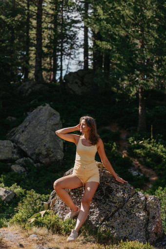 年轻的女人旅游坐着山峰美丽的山景观运动女孩绿色森林山天空湖旅行旅游赶时髦的人女孩山时尚的女人网纹衬衫坐着石头森林旅游热概念徒步旅行旅行夏天神秘的木美丽的自然