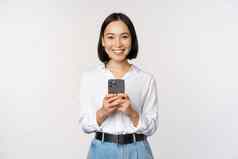 时尚的现代亚洲女孩移动电话应用程序聊天手机微笑站白色上衣工作室背景