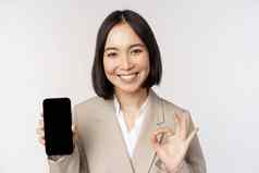 微笑亚洲女人显示智能手机屏幕标志企业人演示了移动电话应用程序接口站白色背景
