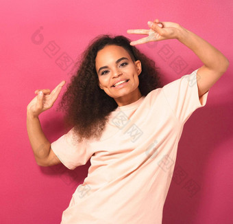年轻的非洲美国女孩非洲式发型头发跳<strong>舞</strong>手势和平手解除积极相机穿桃色的t恤孤立的粉红色的背景美概念<strong>广场</strong>镜头