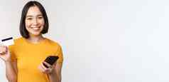 美丽的微笑亚洲女孩信贷卡移动电话支付在线智能手机站黄色的T恤白色背景