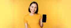 美丽的快乐亚洲女孩显示移动电话屏幕应用程序智能手机小工具站黄色的背景