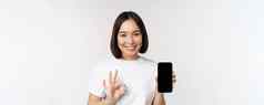 微笑亚洲女人显示移动电话屏幕推荐智能手机应用程序站白色背景