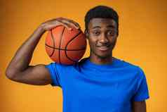 肖像微笑年轻的非洲美国男人。持有篮球黄色的背景