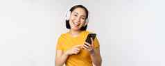 可爱的日本女孩耳机移动电话微笑音乐应用程序智能手机站白色背景