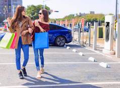 快乐年轻的女人站城市停车电车充电汽车电池小城市站持有购物袋走