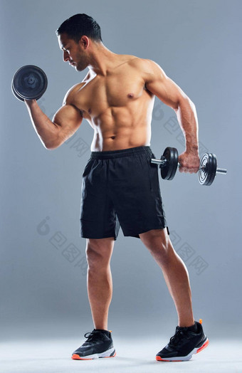 目标使肌肉工作室拍摄肌肉发达的年轻的男人。锻炼哑铃灰色背景