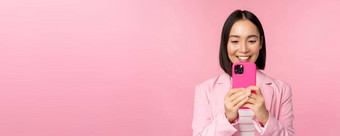 图像微笑亚洲企业女人西装看智能手机应用程序移动电话应用程序站粉红色的背景