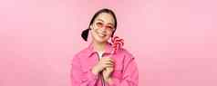微笑亚洲女人太阳镜持有萝莉波普糖果吃糖果快乐站粉红色的背景