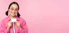 肖像时尚的现代亚洲女孩显示折扣信贷卡很高兴支付非接触式概念购物站粉红色的背景