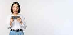 图像年轻的亚洲女人看智能手机应用程序持有移动电话屏幕笑微笑站白色背景