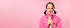 愚蠢的可爱的亚洲女模型舔萝莉波普吃糖果甜蜜的微笑兴奋站粉红色的背景